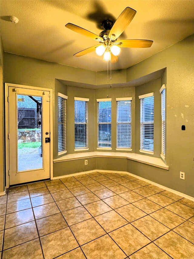 tiled entryway with a textured ceiling, baseboards, and ceiling fan