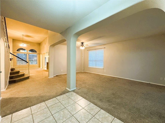 empty room with light carpet, plenty of natural light, stairway, arched walkways, and ceiling fan