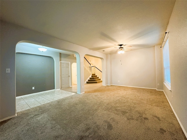 empty room with arched walkways, carpet floors, tile patterned flooring, ceiling fan, and stairs