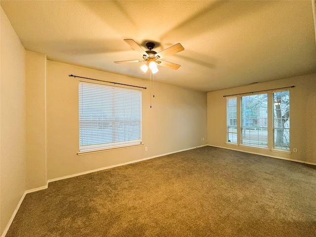 empty room featuring dark colored carpet, baseboards, a textured ceiling, and a ceiling fan