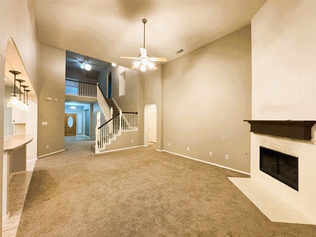 unfurnished living room featuring ceiling fan, carpet, stairs, a tile fireplace, and a high ceiling