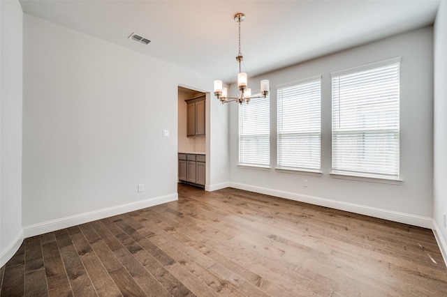 spare room featuring an inviting chandelier, wood finished floors, baseboards, and visible vents