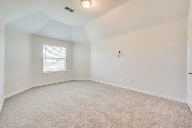 spare room with lofted ceiling, light colored carpet, visible vents, and baseboards