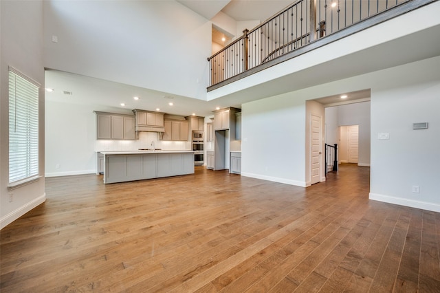 unfurnished living room with baseboards, light wood-type flooring, recessed lighting, a high ceiling, and a sink