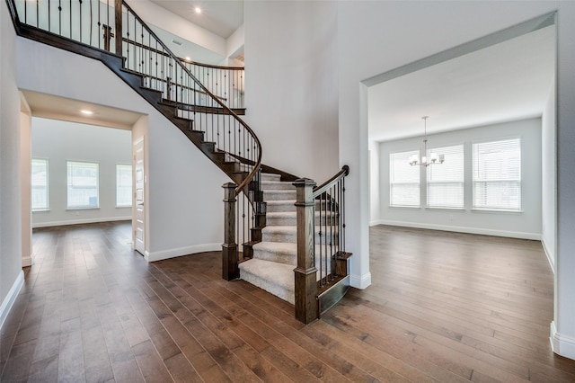 staircase with wood-type flooring, an inviting chandelier, and a healthy amount of sunlight