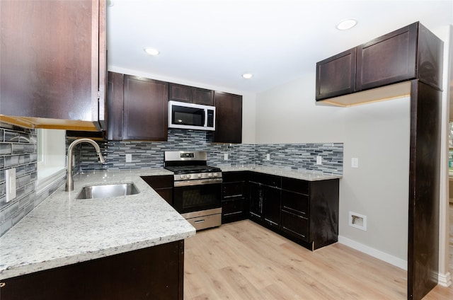 kitchen with white microwave, light wood-style flooring, a sink, stainless steel gas stove, and backsplash