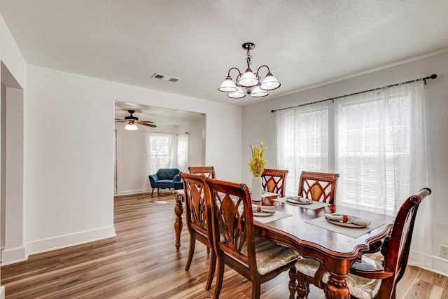 dining space featuring light wood finished floors, visible vents, baseboards, ceiling fan with notable chandelier, and a textured ceiling