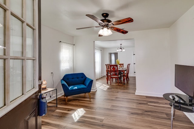 living area featuring baseboards, ceiling fan with notable chandelier, and light wood finished floors