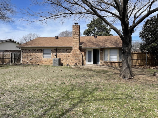 rear view of house featuring brick siding, cooling unit, a chimney, and fence