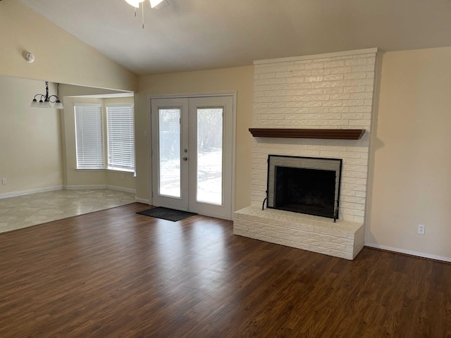 unfurnished living room with wood finished floors, lofted ceiling, a fireplace, french doors, and a notable chandelier