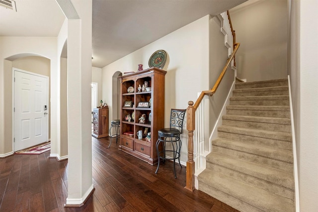 stairs with arched walkways, visible vents, baseboards, and wood-type flooring