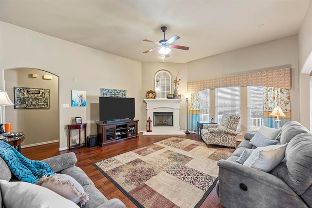 living room featuring a glass covered fireplace, baseboards, wood finished floors, and a ceiling fan