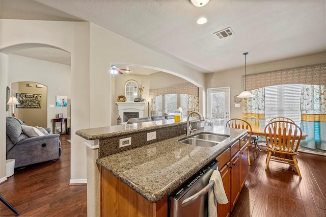 kitchen featuring stainless steel dishwasher, brown cabinetry, open floor plan, and a sink