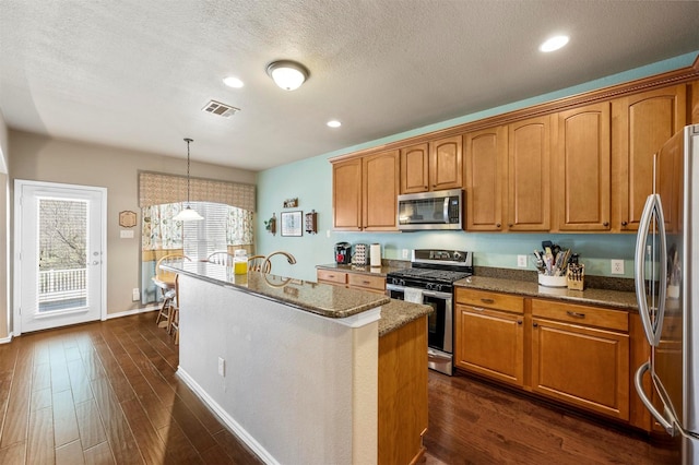 kitchen featuring a center island with sink, appliances with stainless steel finishes, brown cabinets, and dark wood-style flooring