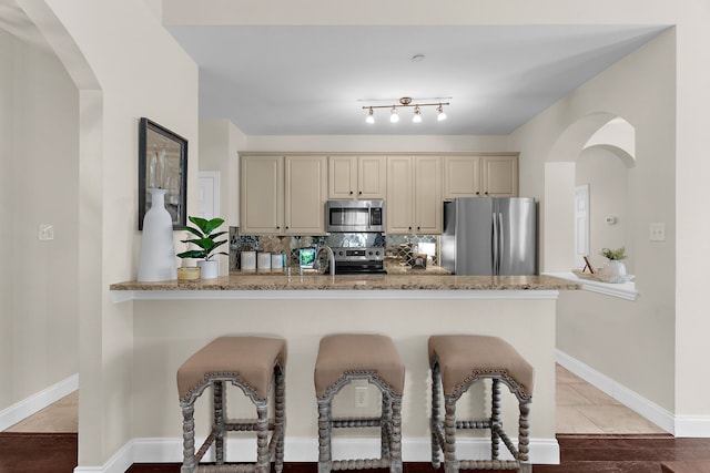 kitchen featuring tasteful backsplash, a breakfast bar, appliances with stainless steel finishes, cream cabinets, and arched walkways