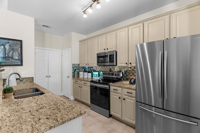 kitchen featuring light stone counters, visible vents, a sink, cream cabinetry, and appliances with stainless steel finishes