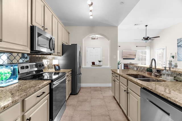 kitchen featuring decorative backsplash, appliances with stainless steel finishes, arched walkways, cream cabinetry, and a sink