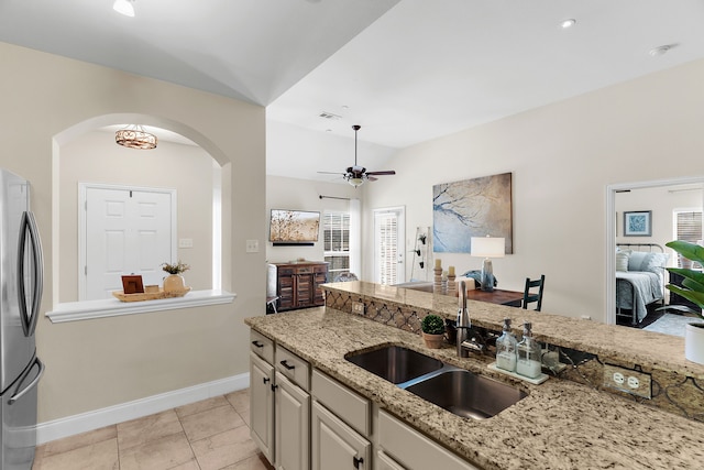 kitchen with light stone countertops, a ceiling fan, arched walkways, freestanding refrigerator, and a sink