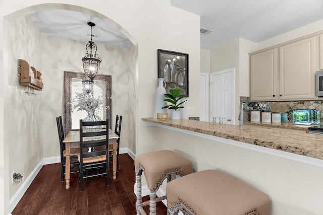 dining room featuring dark wood-type flooring, visible vents, arched walkways, and baseboards