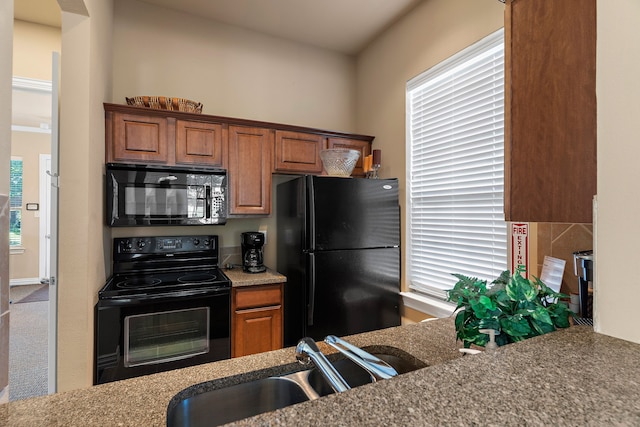 kitchen with a sink, brown cabinets, arched walkways, and black appliances