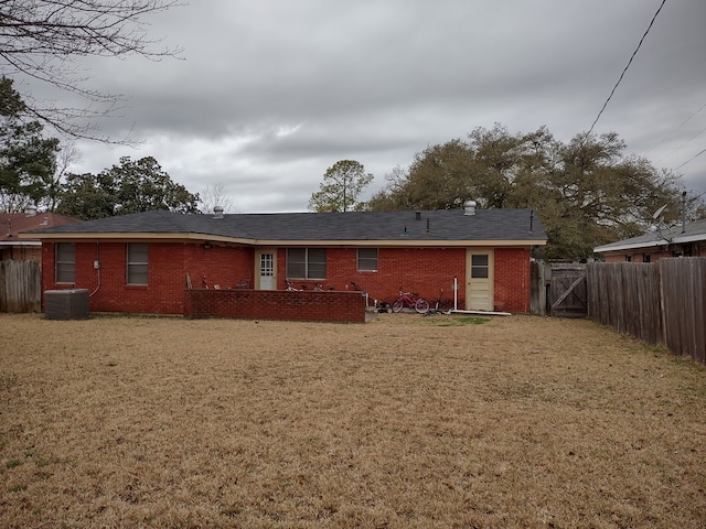 rear view of house featuring brick siding, fence, central air condition unit, a lawn, and a gate