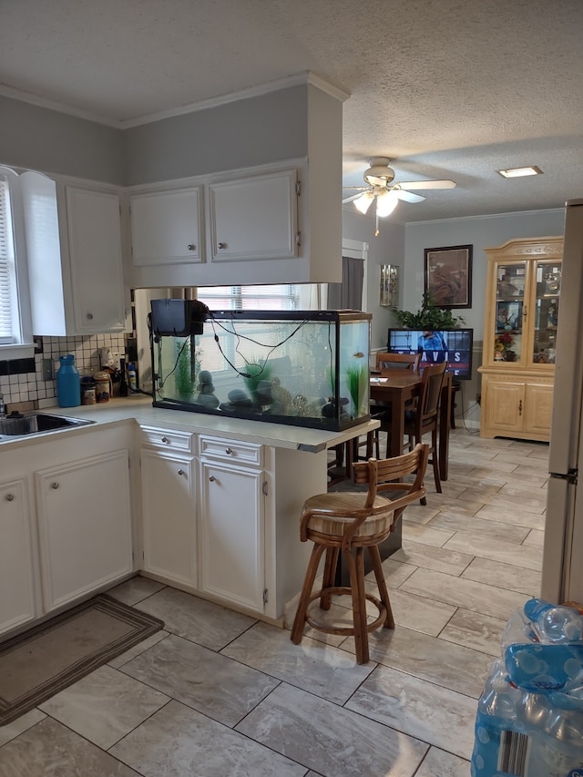 kitchen featuring decorative backsplash, white cabinets, freestanding refrigerator, and ceiling fan