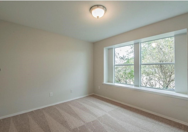 spare room featuring light colored carpet and baseboards