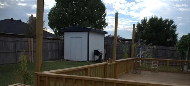 deck featuring a storage shed, a fenced backyard, an outbuilding, and a grill