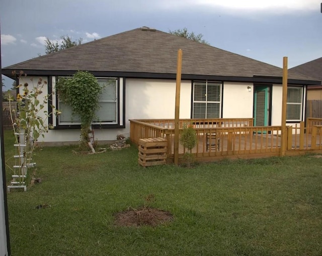 rear view of property with a deck, a yard, roof with shingles, and stucco siding