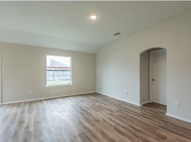 spare room featuring visible vents, baseboards, lofted ceiling, wood finished floors, and arched walkways