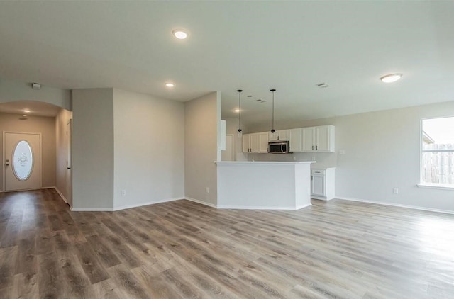 unfurnished living room with recessed lighting, light wood-style floors, arched walkways, and baseboards