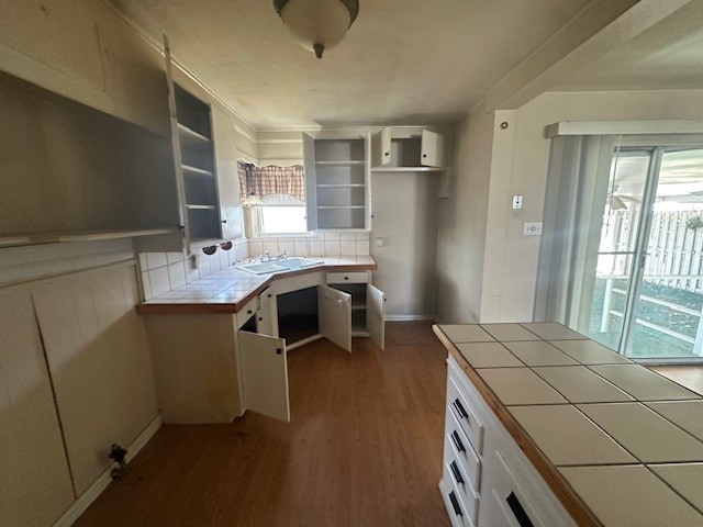 kitchen featuring tile countertops, wood finished floors, a sink, white cabinetry, and tasteful backsplash