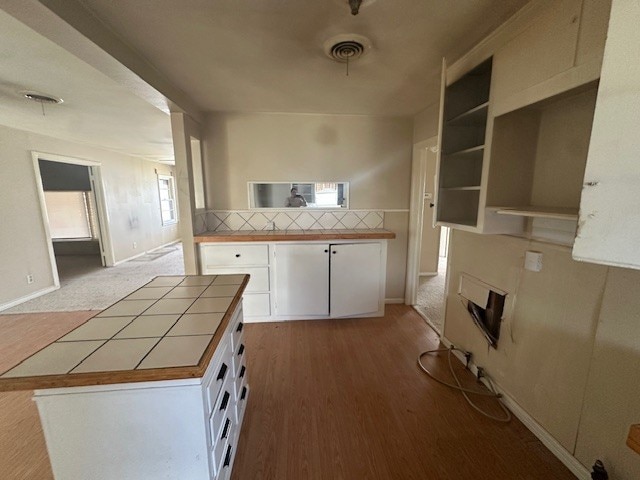 kitchen with visible vents, tile countertops, wood finished floors, white cabinetry, and open shelves