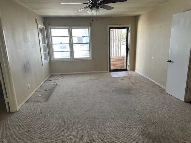 interior space featuring light colored carpet, baseboards, and ceiling fan