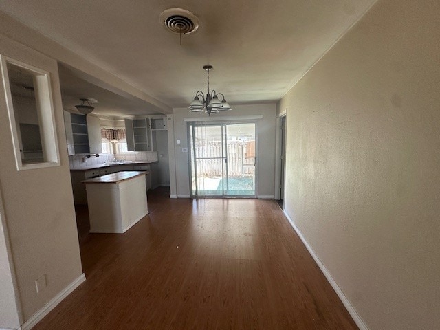 unfurnished dining area featuring dark wood finished floors, an inviting chandelier, baseboards, and visible vents