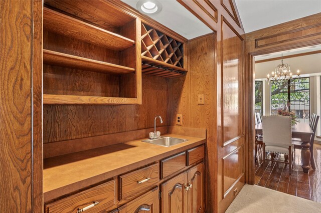 kitchen featuring brown cabinets, dark wood-type flooring, a sink, an inviting chandelier, and light countertops