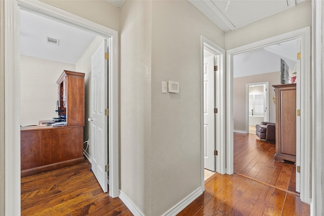 hall featuring visible vents, baseboards, and dark wood-style flooring