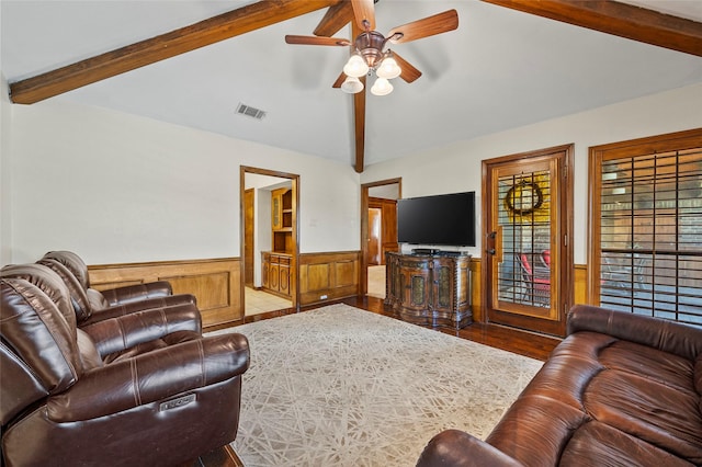 living area featuring wood finished floors, a ceiling fan, visible vents, vaulted ceiling with beams, and wainscoting