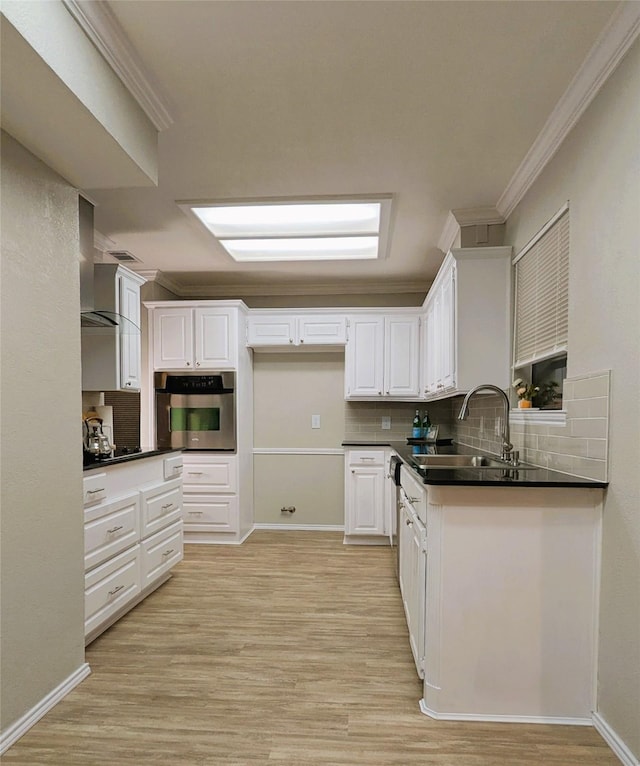 kitchen featuring oven, ornamental molding, a sink, dark countertops, and white cabinets