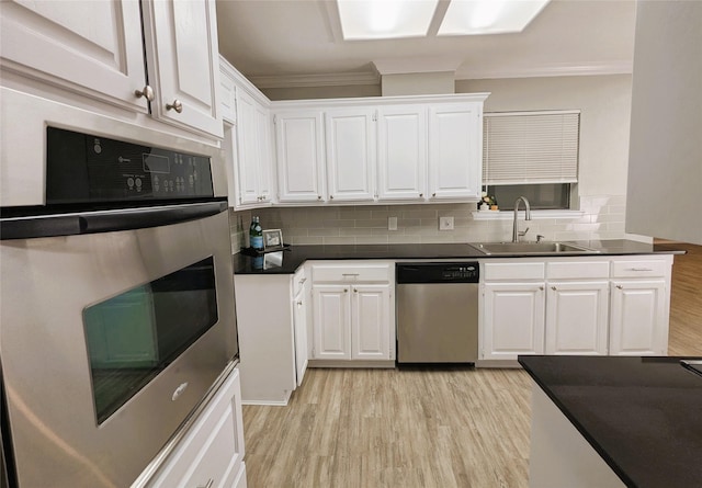 kitchen with a sink, white cabinets, light wood-style floors, appliances with stainless steel finishes, and dark countertops