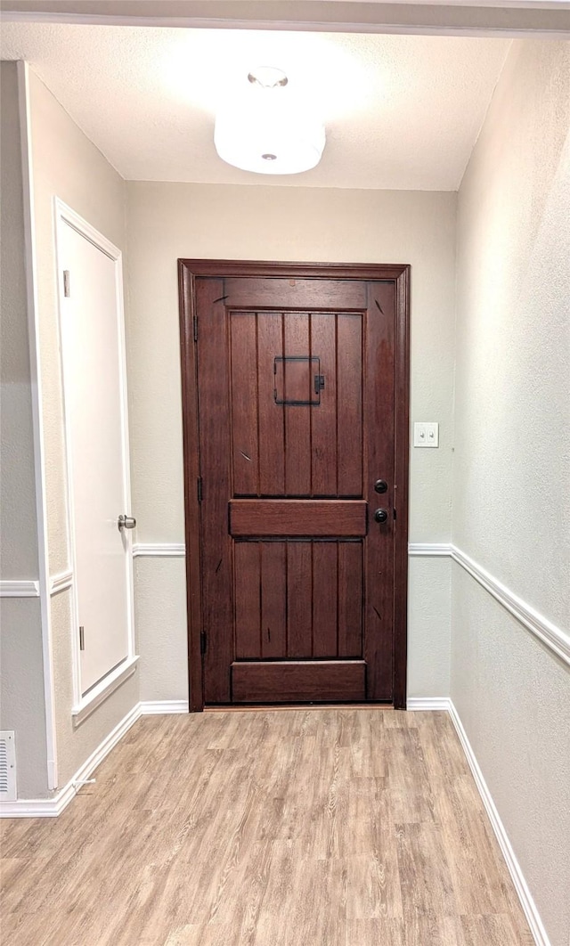 doorway to outside featuring light wood-style floors, baseboards, and a textured ceiling