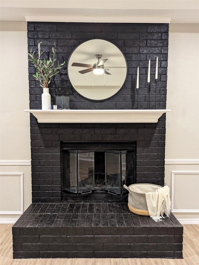 details featuring a wainscoted wall, wood finished floors, a brick fireplace, and ceiling fan