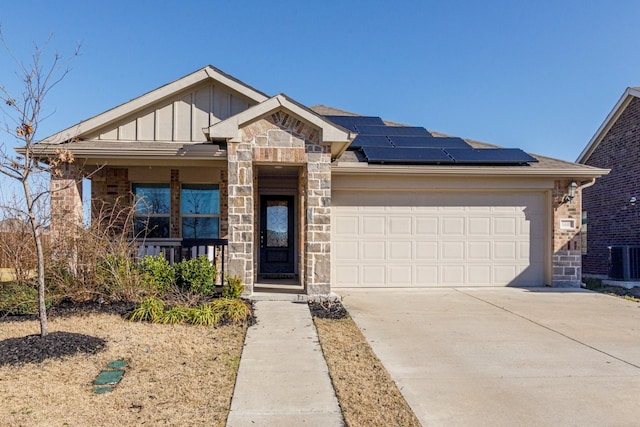 view of front of house with an attached garage, concrete driveway, stone siding, board and batten siding, and roof mounted solar panels