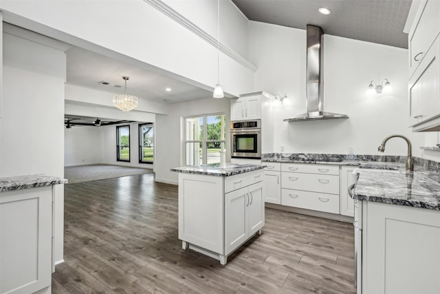 kitchen with dark stone counters, wall chimney range hood, light wood-style flooring, and a sink