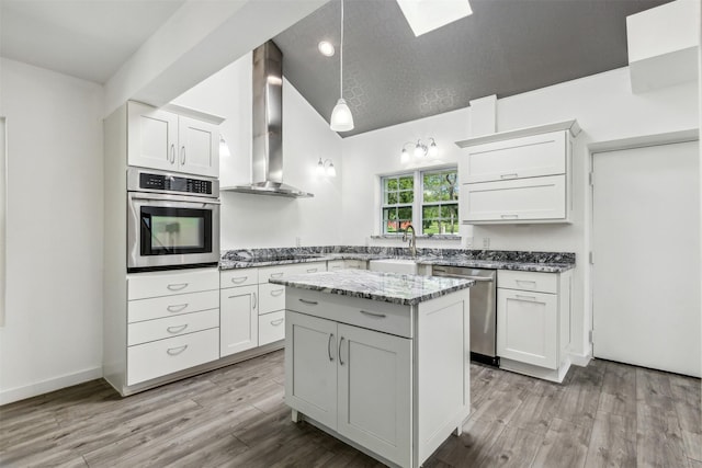 kitchen with white cabinetry, appliances with stainless steel finishes, light wood-type flooring, and wall chimney exhaust hood