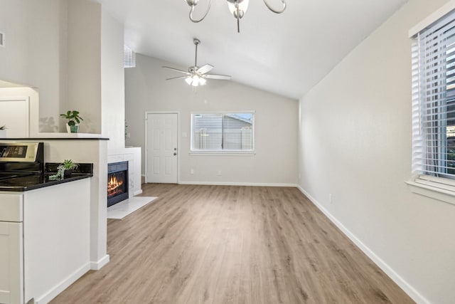 unfurnished living room with vaulted ceiling, a fireplace with flush hearth, light wood finished floors, baseboards, and ceiling fan