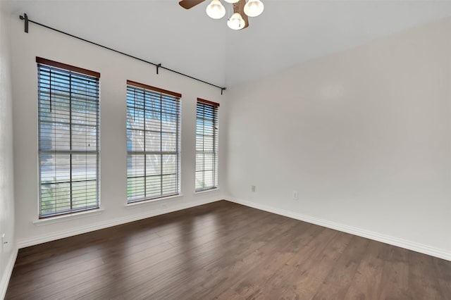 spare room with a ceiling fan, vaulted ceiling, dark wood-style floors, and baseboards