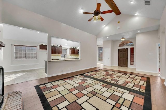 unfurnished living room with visible vents, high vaulted ceiling, ceiling fan, beamed ceiling, and light wood-type flooring