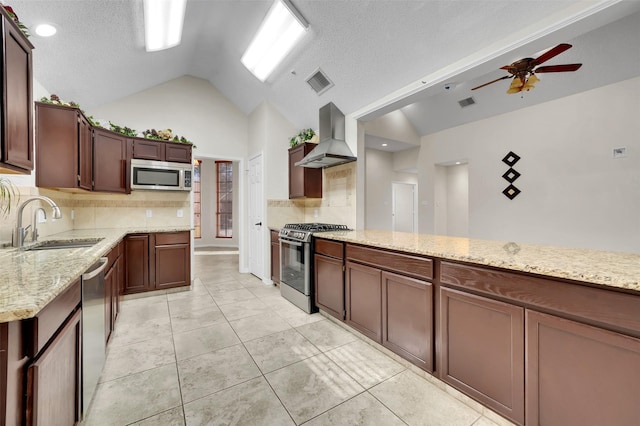 kitchen featuring ceiling fan, a sink, vaulted ceiling, appliances with stainless steel finishes, and wall chimney exhaust hood