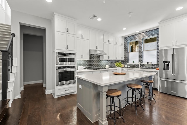 kitchen featuring under cabinet range hood, decorative backsplash, appliances with stainless steel finishes, and light countertops